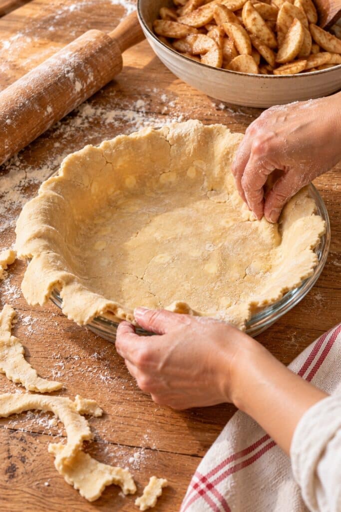 Rolled pie dough eased into a glass pie plate with the edge hanging over the rim