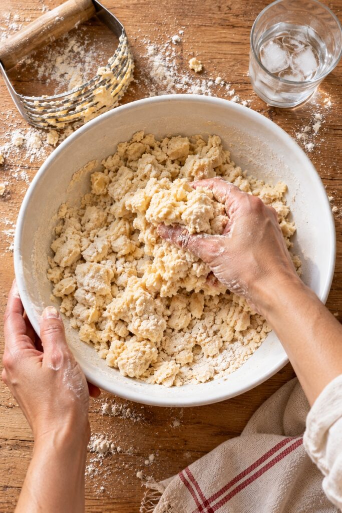 Pie dough crumbs with pea-sized pieces of butter being squeezed together by hand
