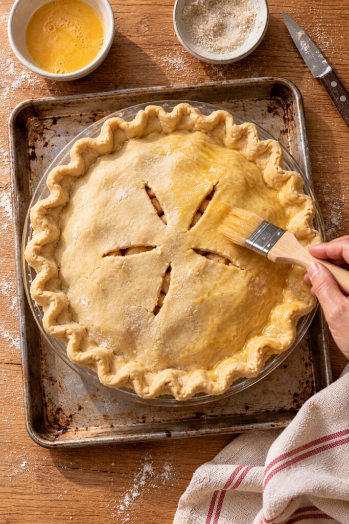 Unbaked apple pie with a crimped edge, vent slits and egg wash ready for the oven